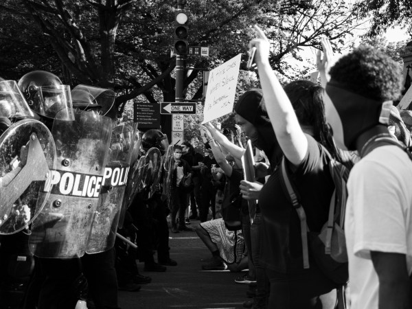 A line of protesters with signs standing in a street, just feet from a line of police with riot shields.