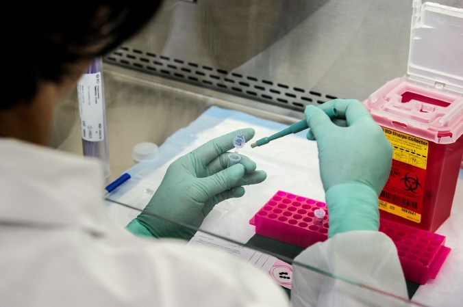 Gloved hands testing a COVID-19 sample in a lab