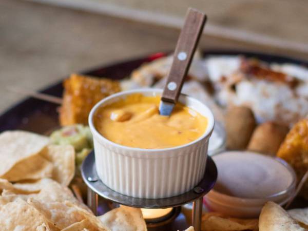 Bowl of cheese sauce in a large plate of nachos.