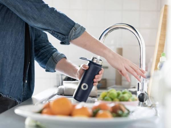 Person filling up water bottle at kitchen sink with tap water.