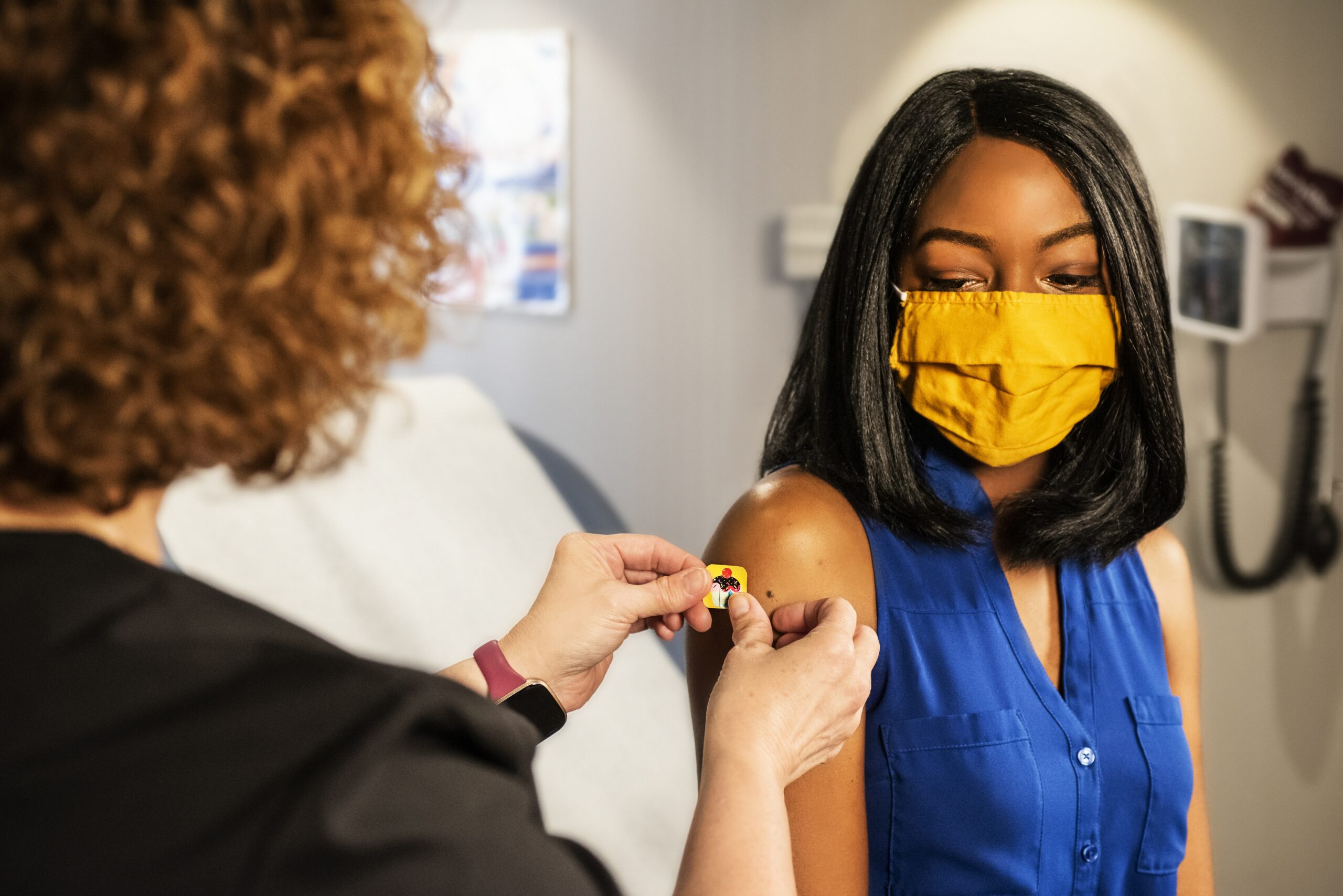 Doctor administering COVID-19 vaccine to masked patient in medical office.