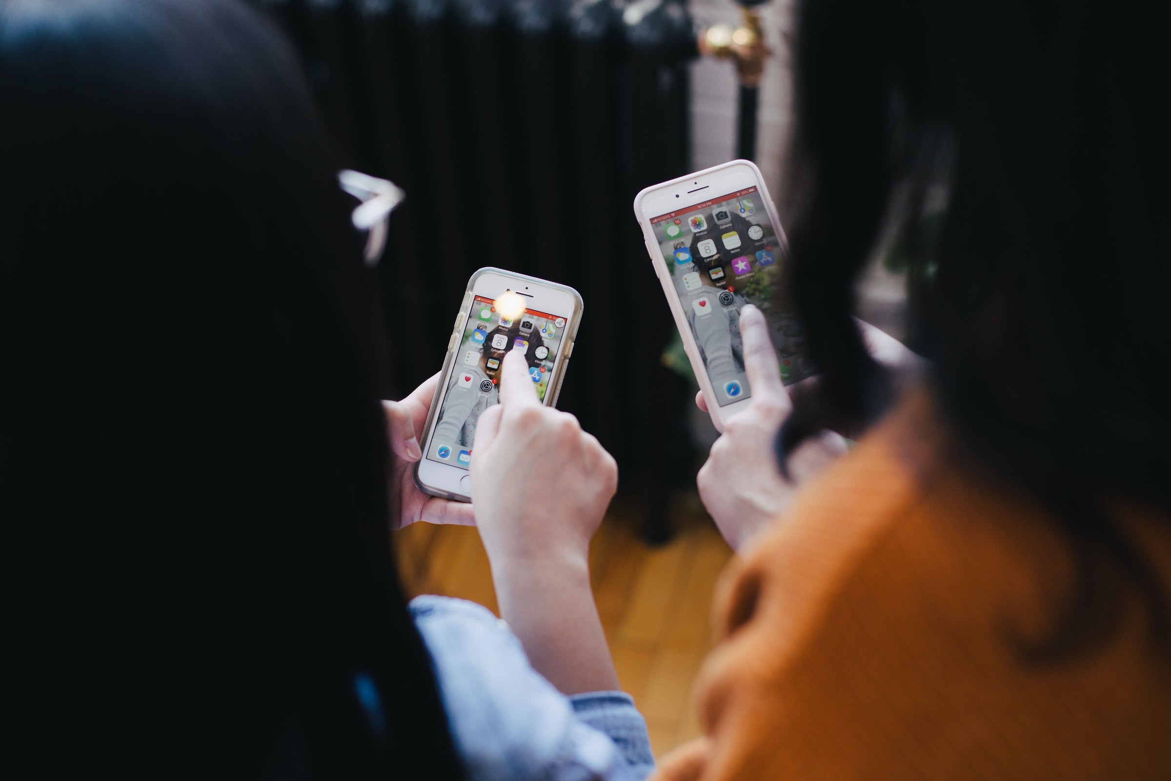 Two people facing away from the camera while pointing at their iPhones.