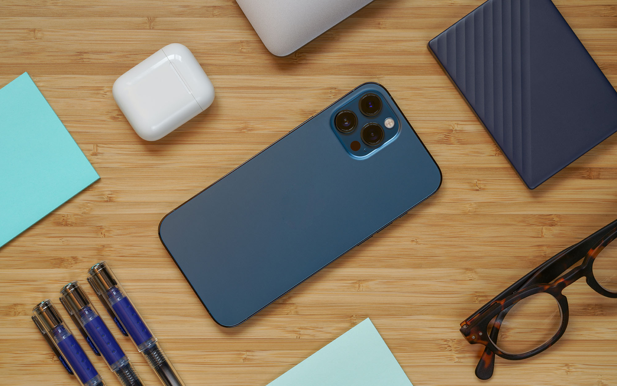 iphone 12 in one of the best iphone cases, glasses, pens, airpods, and hard drive on a wooden surface