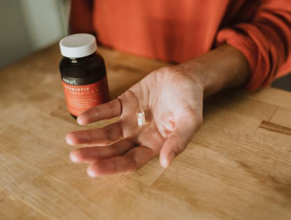 Person in an orange shift holding a white probiotic pull next to a brown vitamin bottle