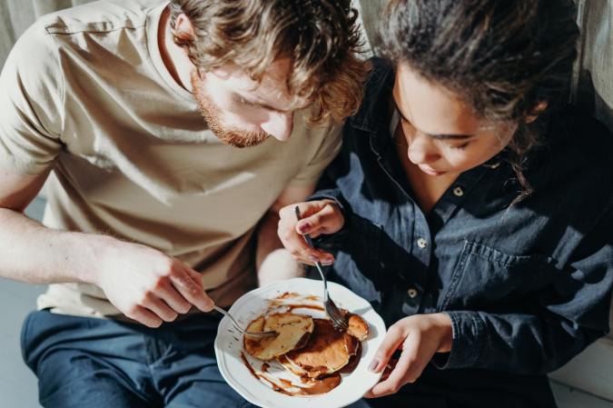 a man and woman sit close to each other and share a plate of pancakes