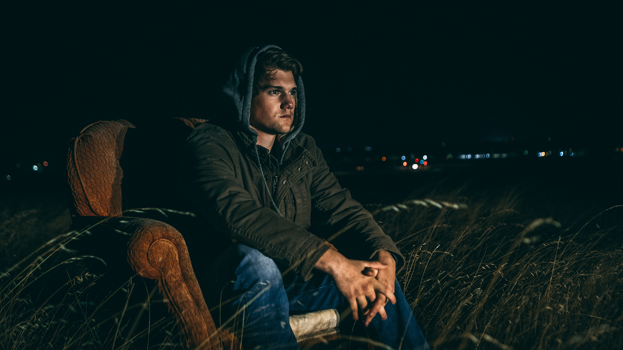 man in a hoodie sitting in an old armchair outside watching an outdoor tv