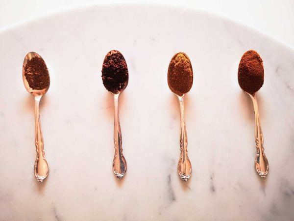 Four gold spoons with reddish spice blends on a marble table