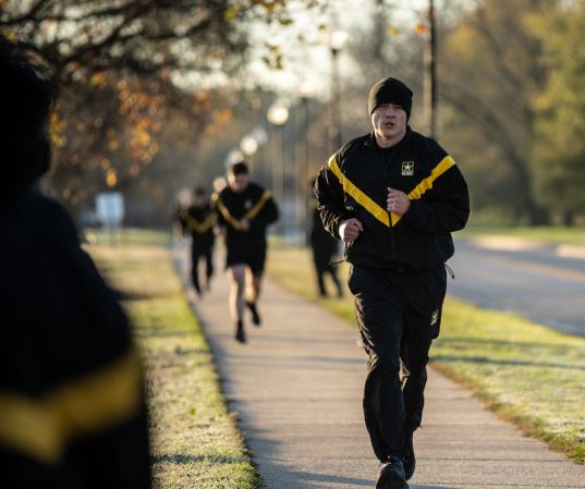 Army cadet running in a black and yellow sweatsuit on a sidewalk