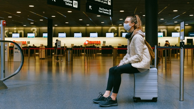 Traveler sits on suitcase in airport.