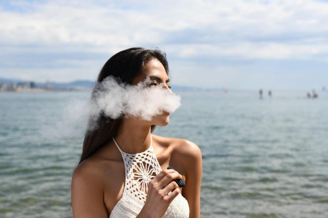 Model with long brown hair along the water using a vape pen