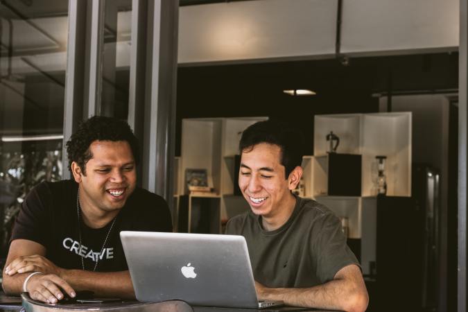 Two young brown people at a Mac laptop