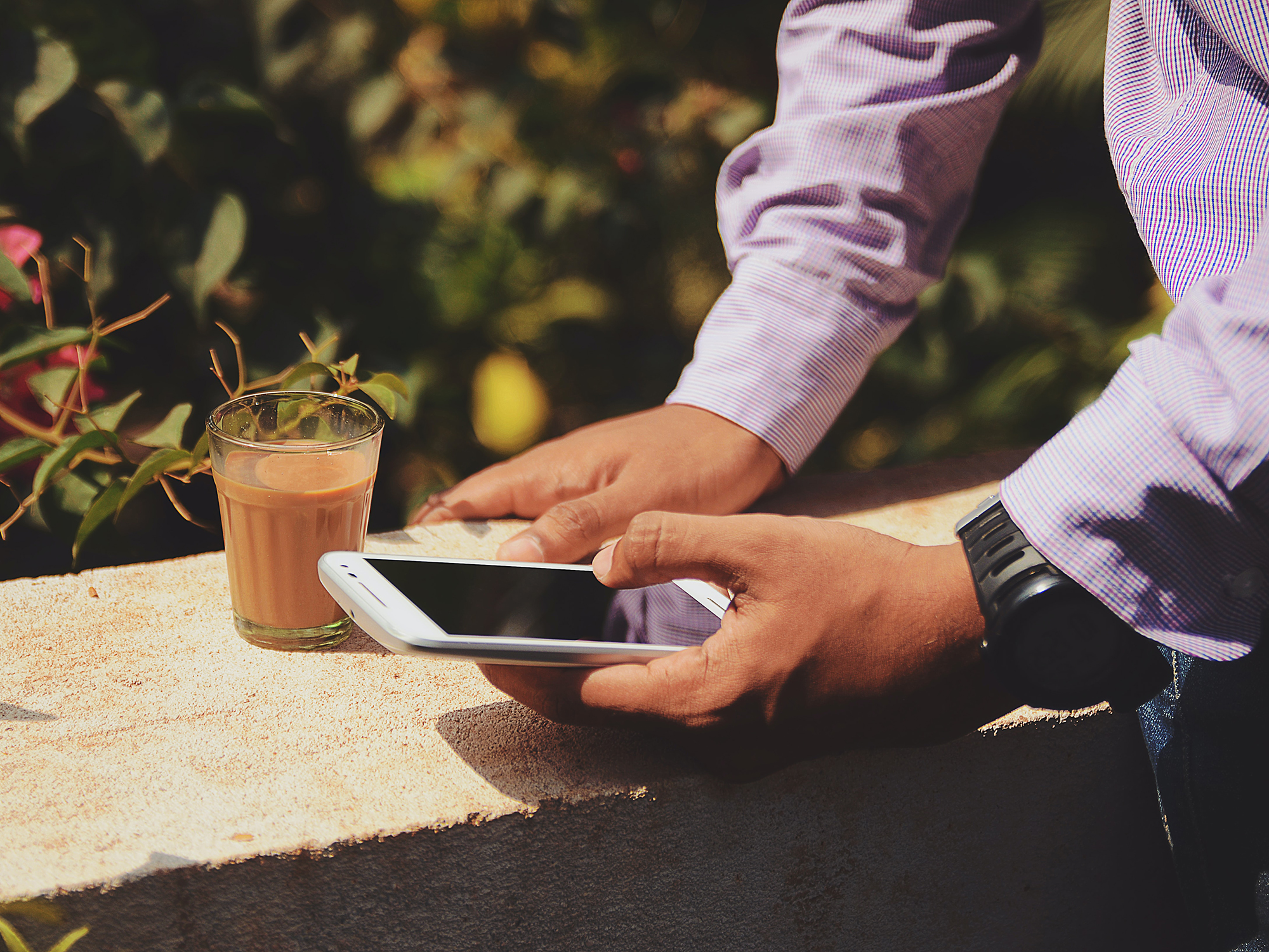 A person standing outside bear a concrete wall, holding their phone with a coffee nearby.