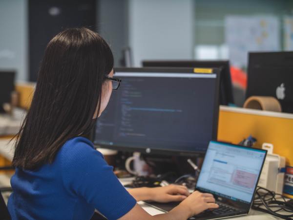 A person sitting in front of a desktop computer in an office, using a laptop. She should learn to schedule a shutdown on Windows.