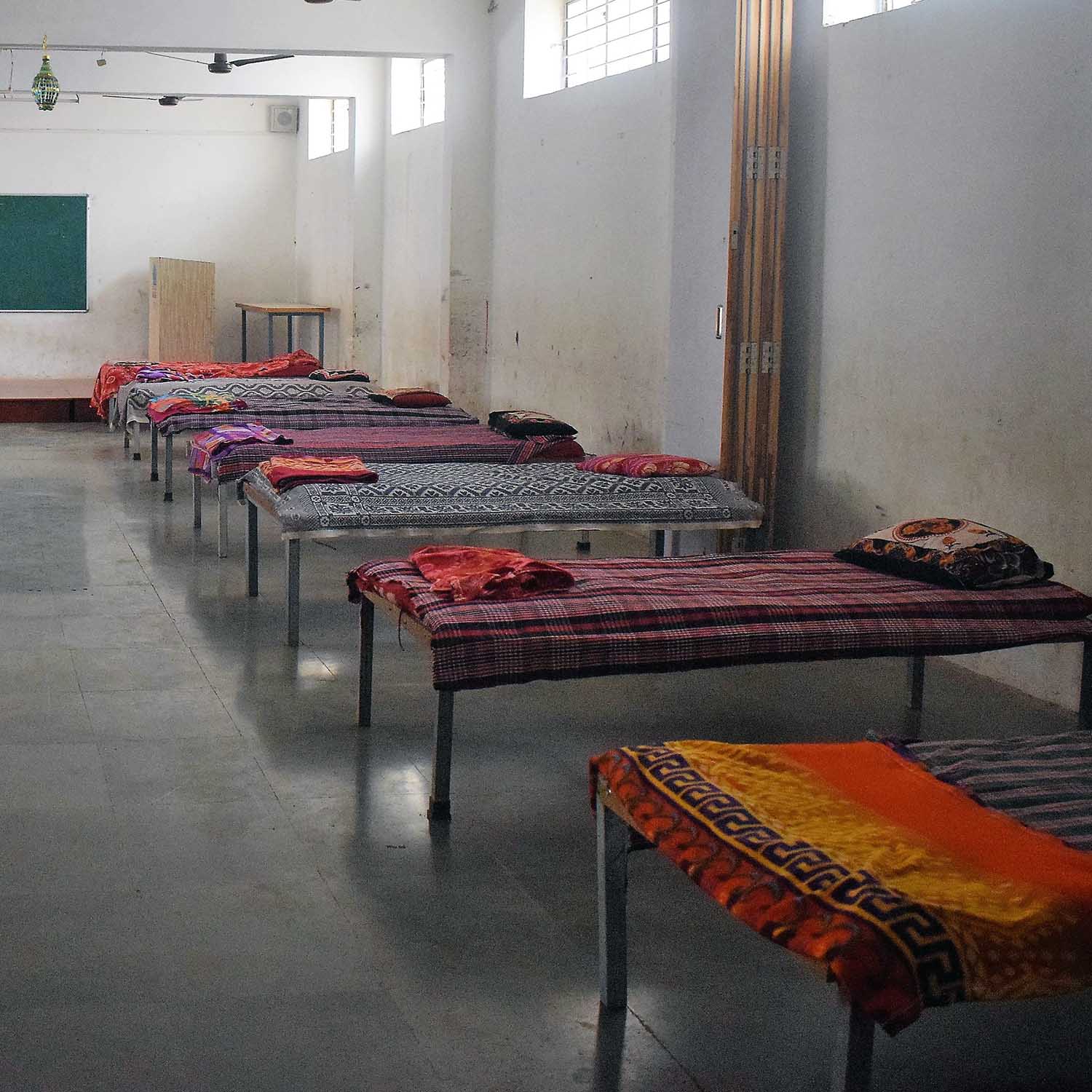 Cots with blankets in a classroom with a stone floor