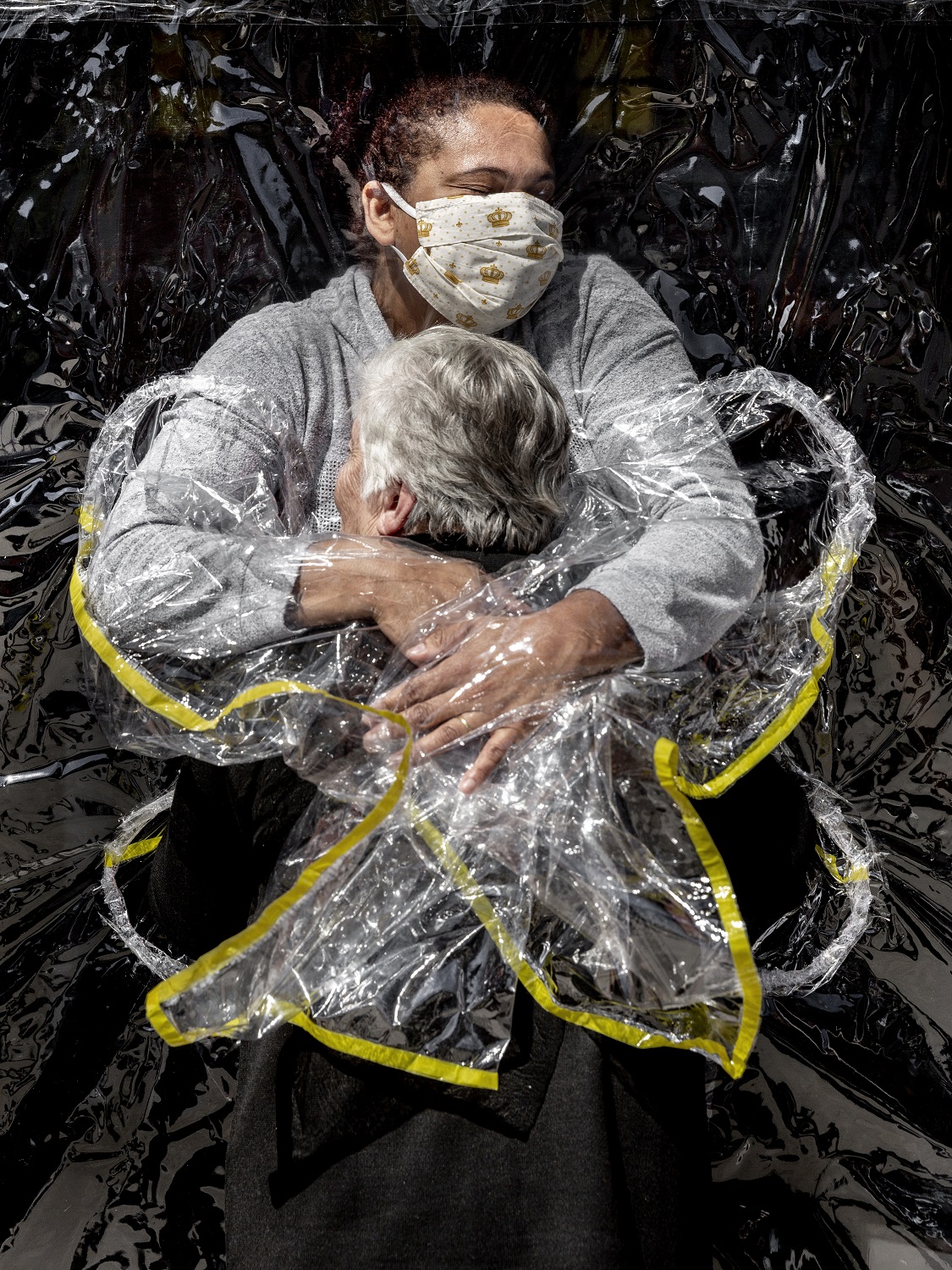 Old woman and person in mask hugging through PPE