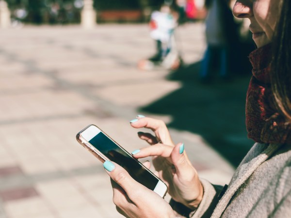 A person standing on a sidewalk outside while using their phone.