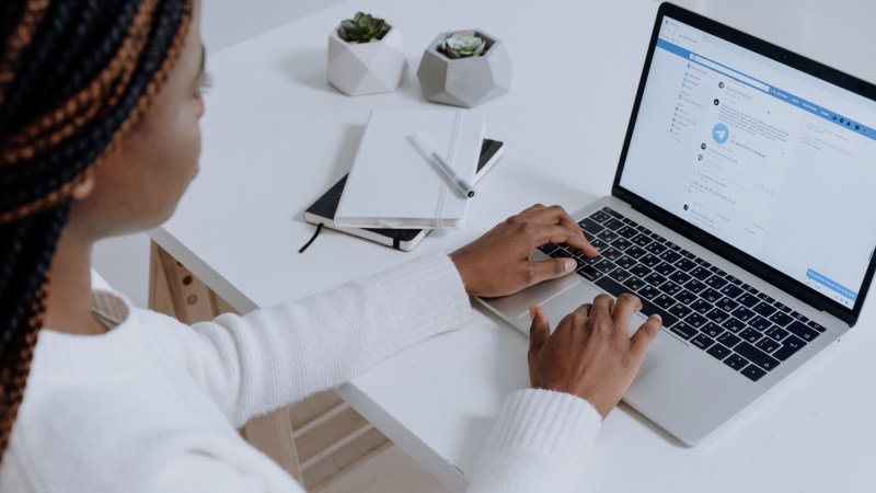 A woman in a white long-sleeved shirt sitting in front of a Macbook laptop at a white table, looking at her Facebook News Feed, maybe thinking about cleaning it up.