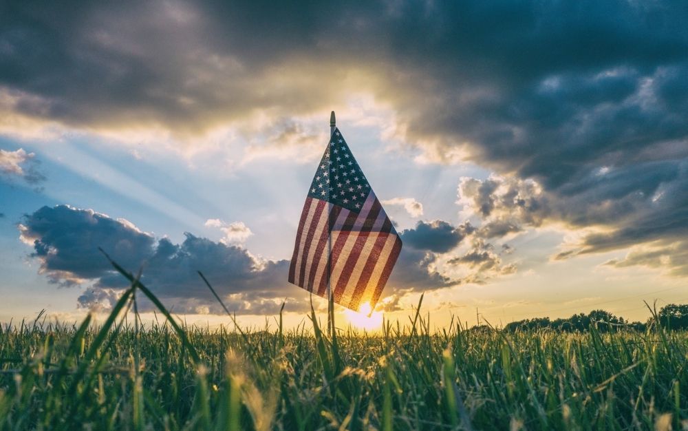 A USA flag waving under the sunset in a large green field.
