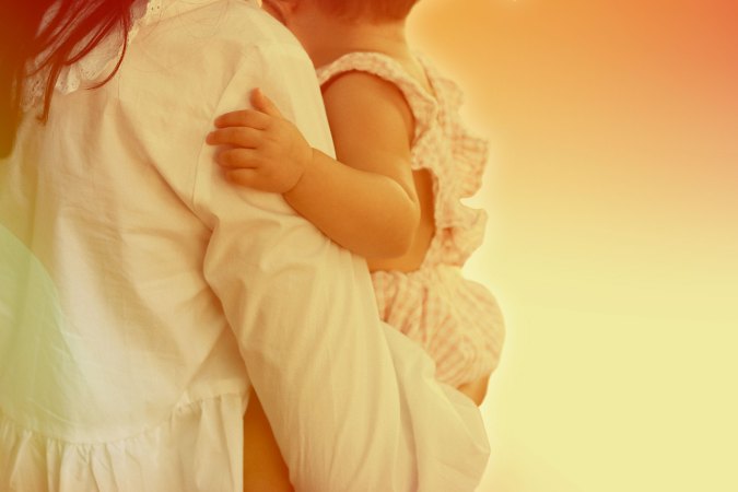 A person wearing a long-sleeved white shirt while holding a baby.