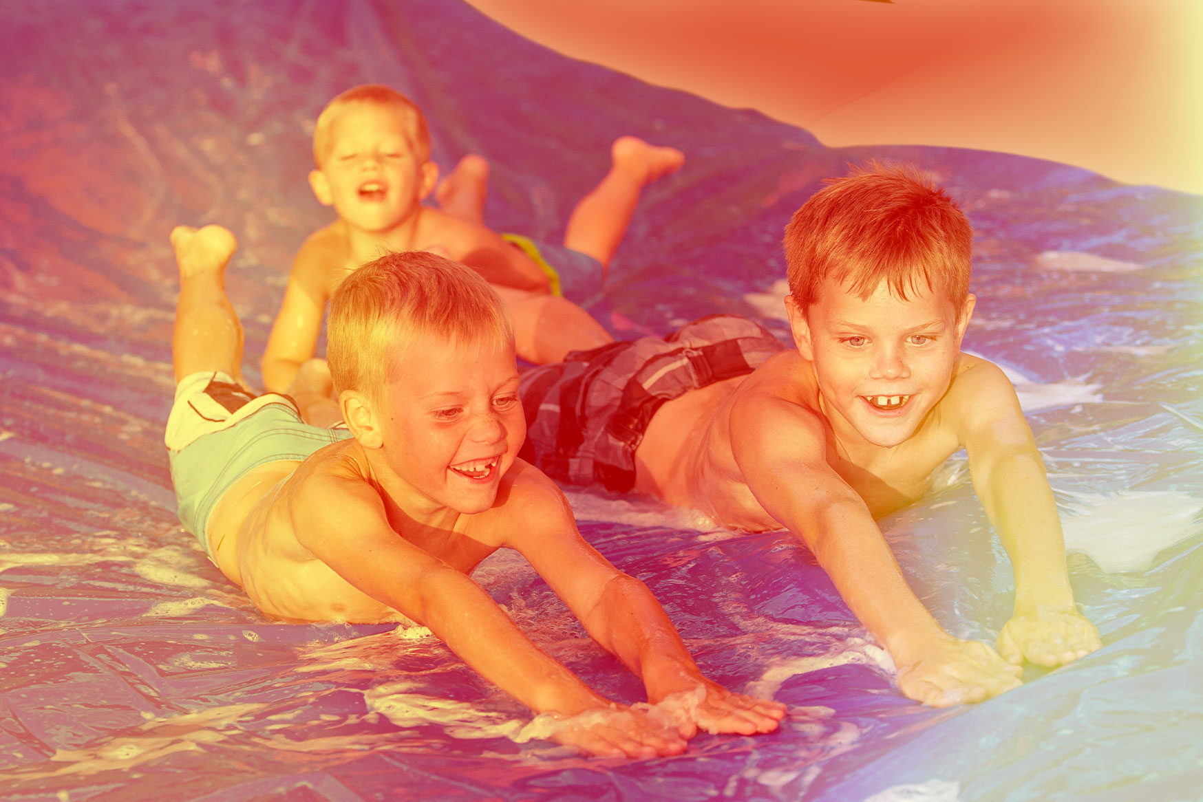 Three children sliding down a slip and slide.