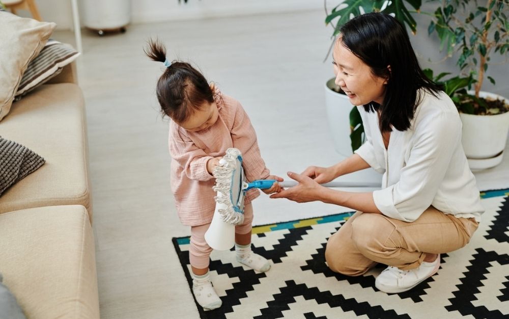 A mother smiling with her child and showing her a a cloth with white cloth and long tail, standing on a black and white carpet.