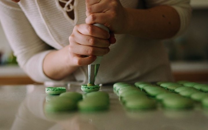 Two hands while holding in them a small machine for filling sweets placed on the table.