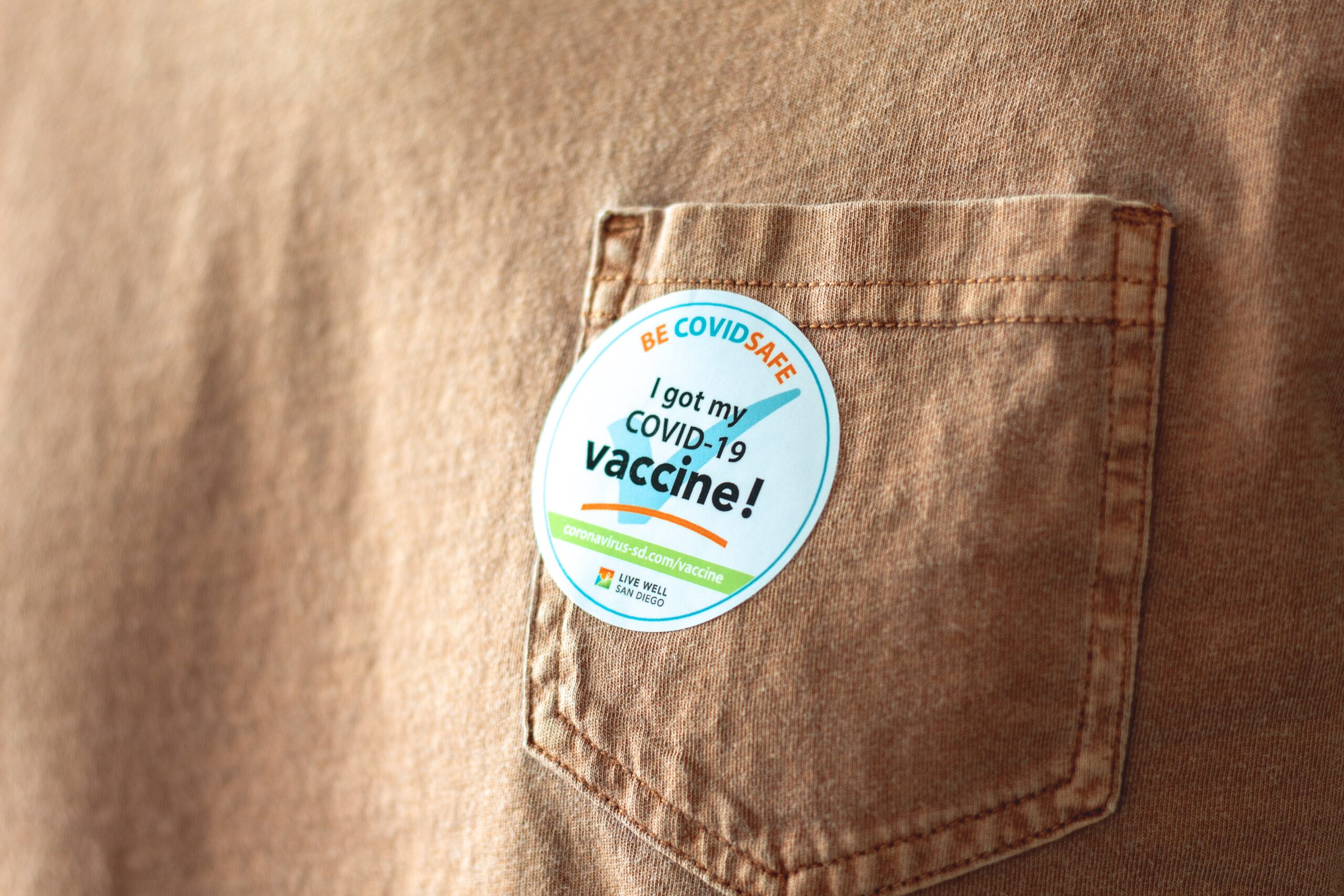 A sticker placed on the pocket of a brown tee shirt, which reads: I got my COVID-19 vaccine.