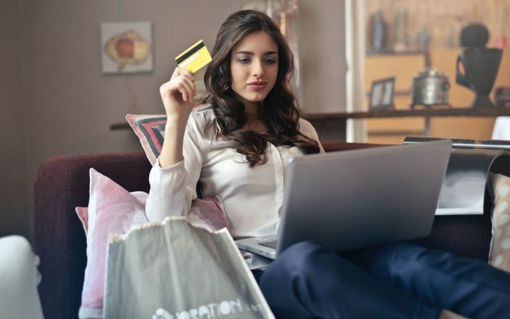 A girl with a white skirt holding in her hands a yellow card in front of her laptop.