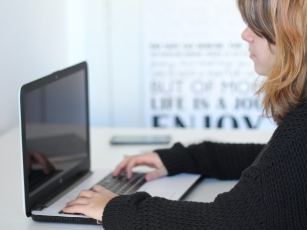 A person sitting at a table in an office, typing on a laptop computer.