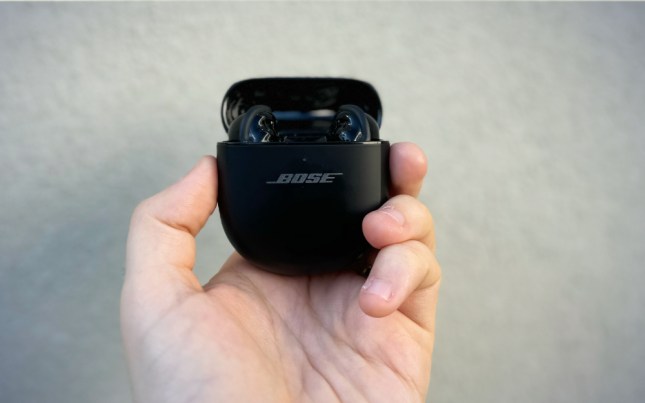 A pesron holding a pair Bose QuietComfort Ultimate against a plain wall.