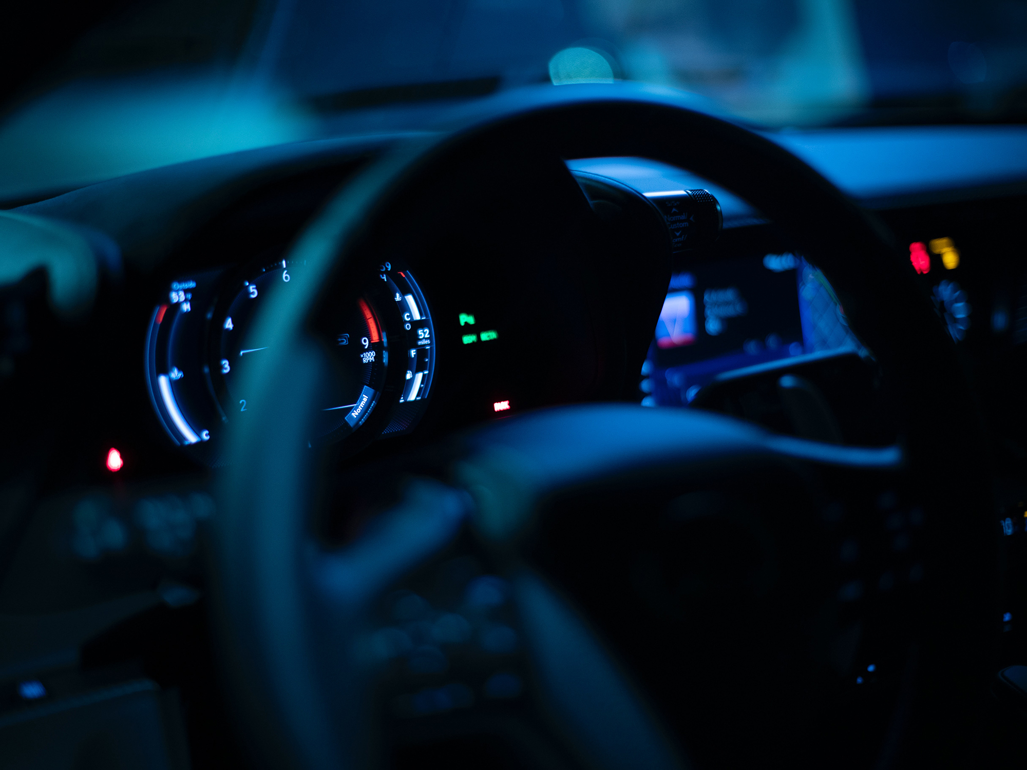 The steering wheel and dashboard of a car at night.