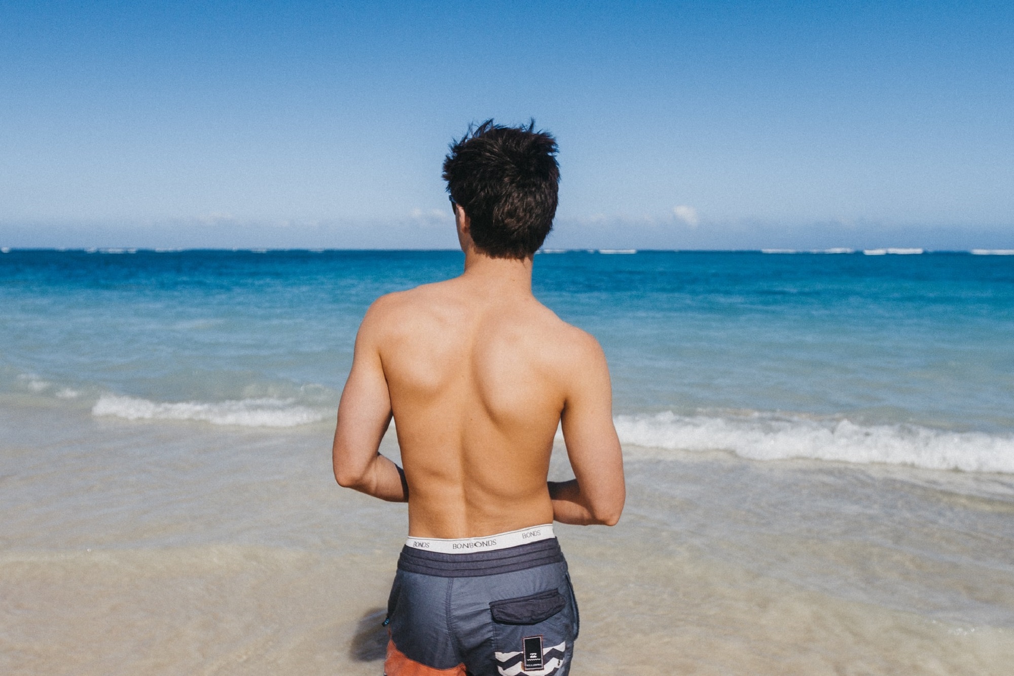 Shirtless person looking out at the ocean and beach