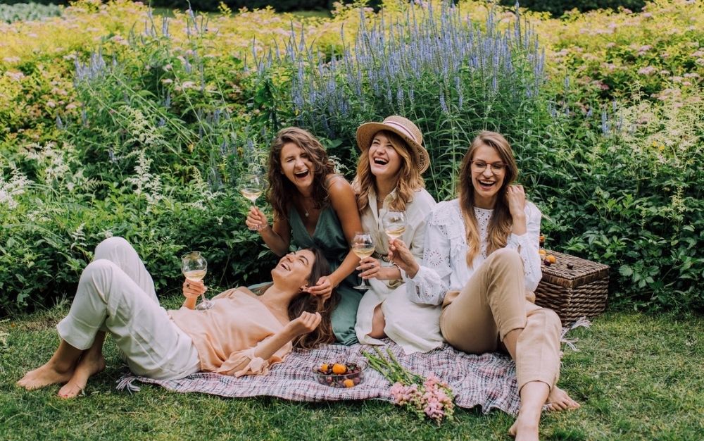 Four girls sitting and smiling with each other while in their hands are wine glasses.