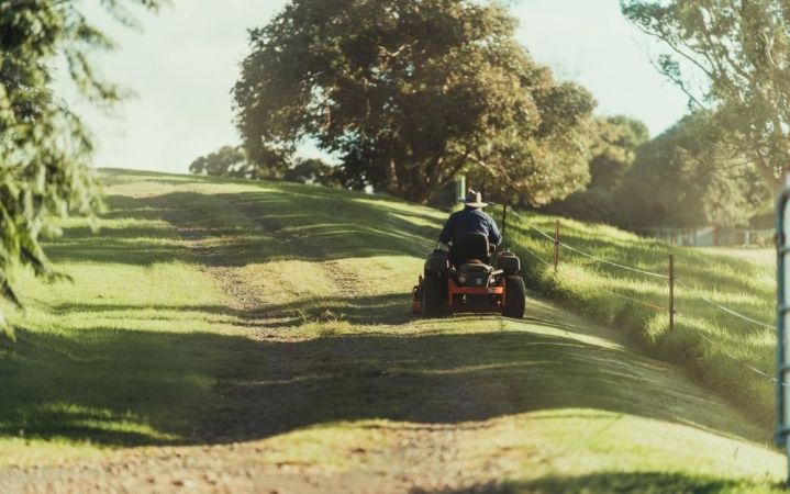 A man riding a mower in the middle of a green grass field with sunlight falling on it.