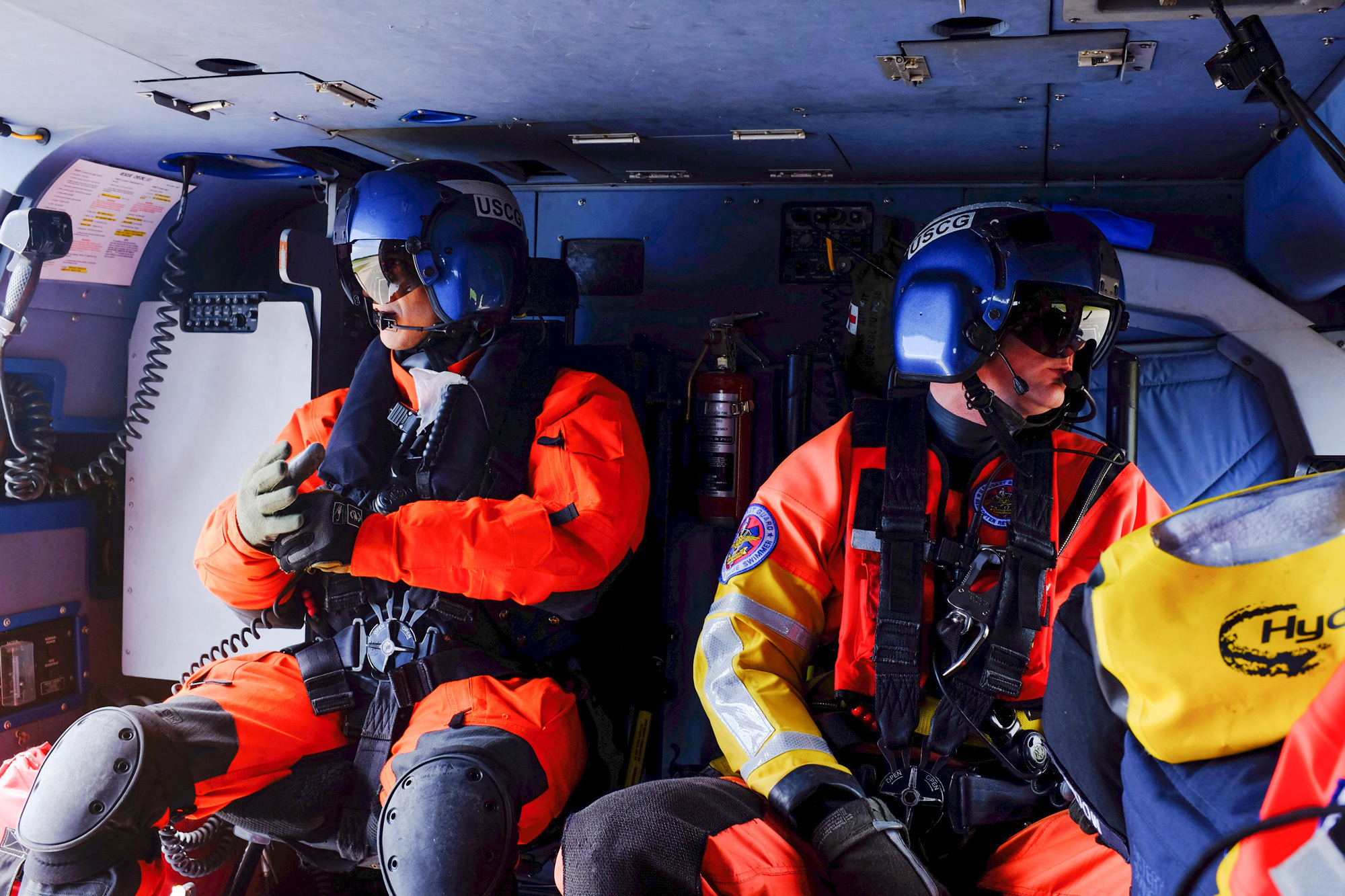 Two members of the Coast Guard ride in the back of a helicopter