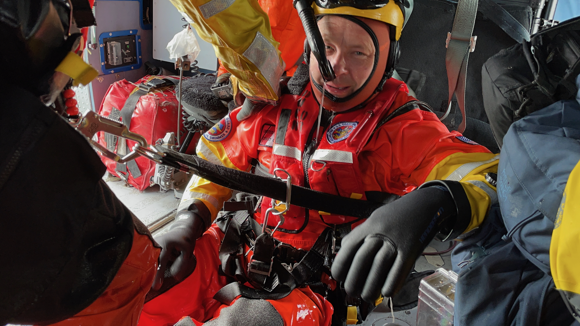 A member of the Coast Guard sits on the floor of a helicopter