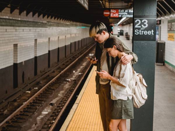 Couple waits by the NYC train platform looking at their phones