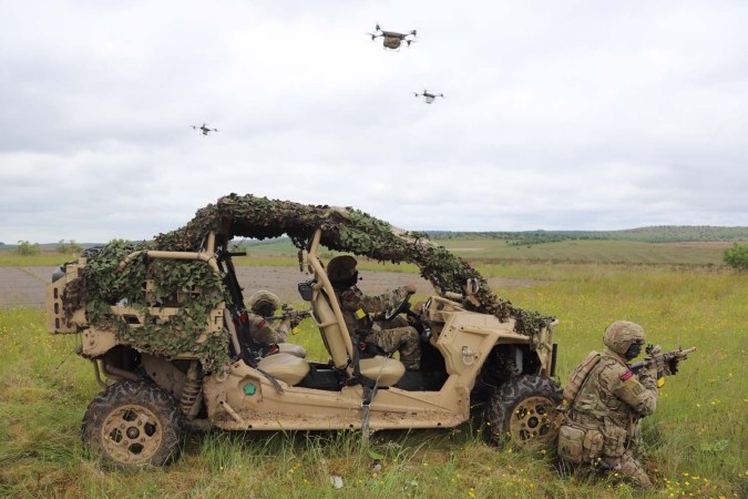 soldiers near a vehicle with drones in the background