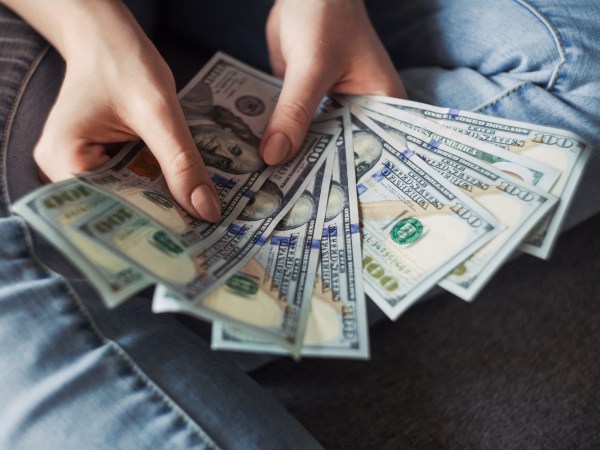 A person sitting on the floor, holding several $100 bills in a fan shape.