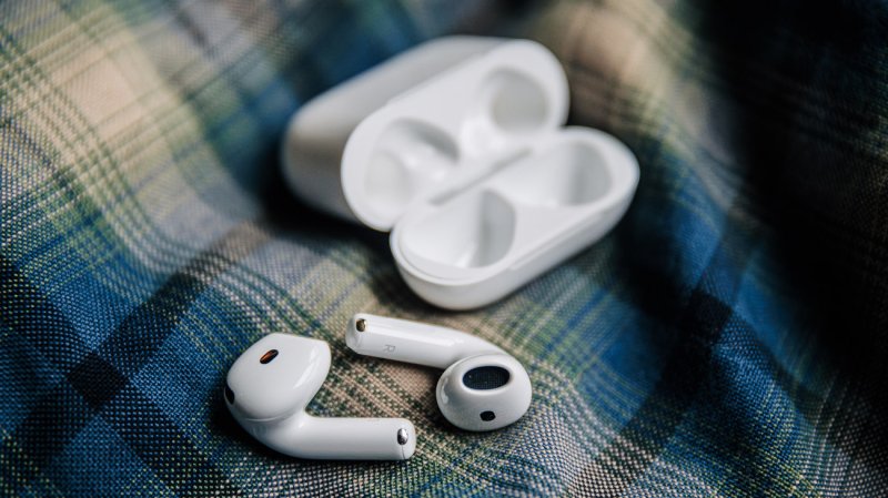  White AirPods 4 earbuds with noise cancellation and an AirPods 4 case sitting on a blue flannel shirt