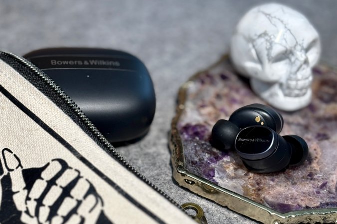  Black Bowers & Wilkins Pi8 true wireless earbuds shown on an amethyst coaster next to a marble skull decoration