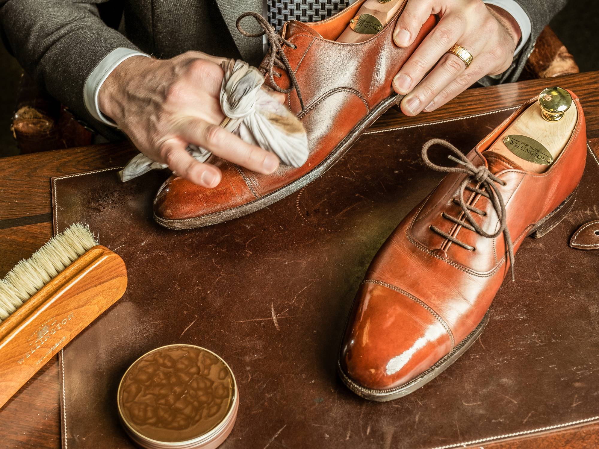 Hands polishing fancy leather shoes on a fancy wooden table.