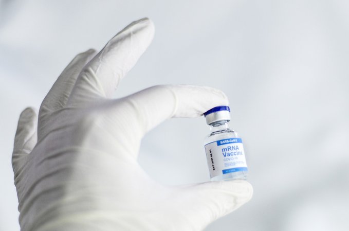 A gloved hand holds a vial of COVID vaccine.