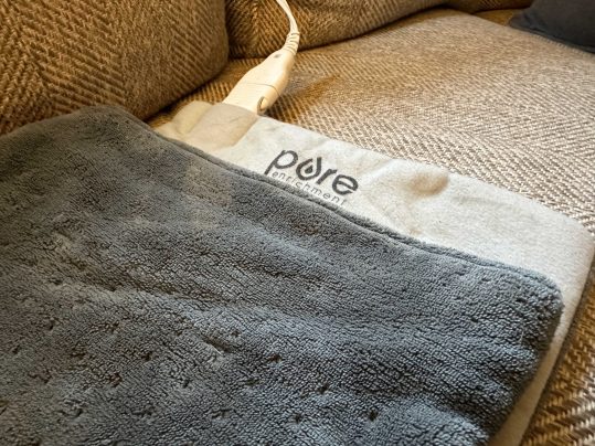 A gray heating pad made by Pure Enrichment with some cords on a couch