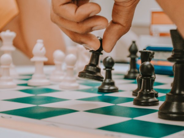 Two people playing chess on a green-and-white board. One person is moving a black bishop piece.