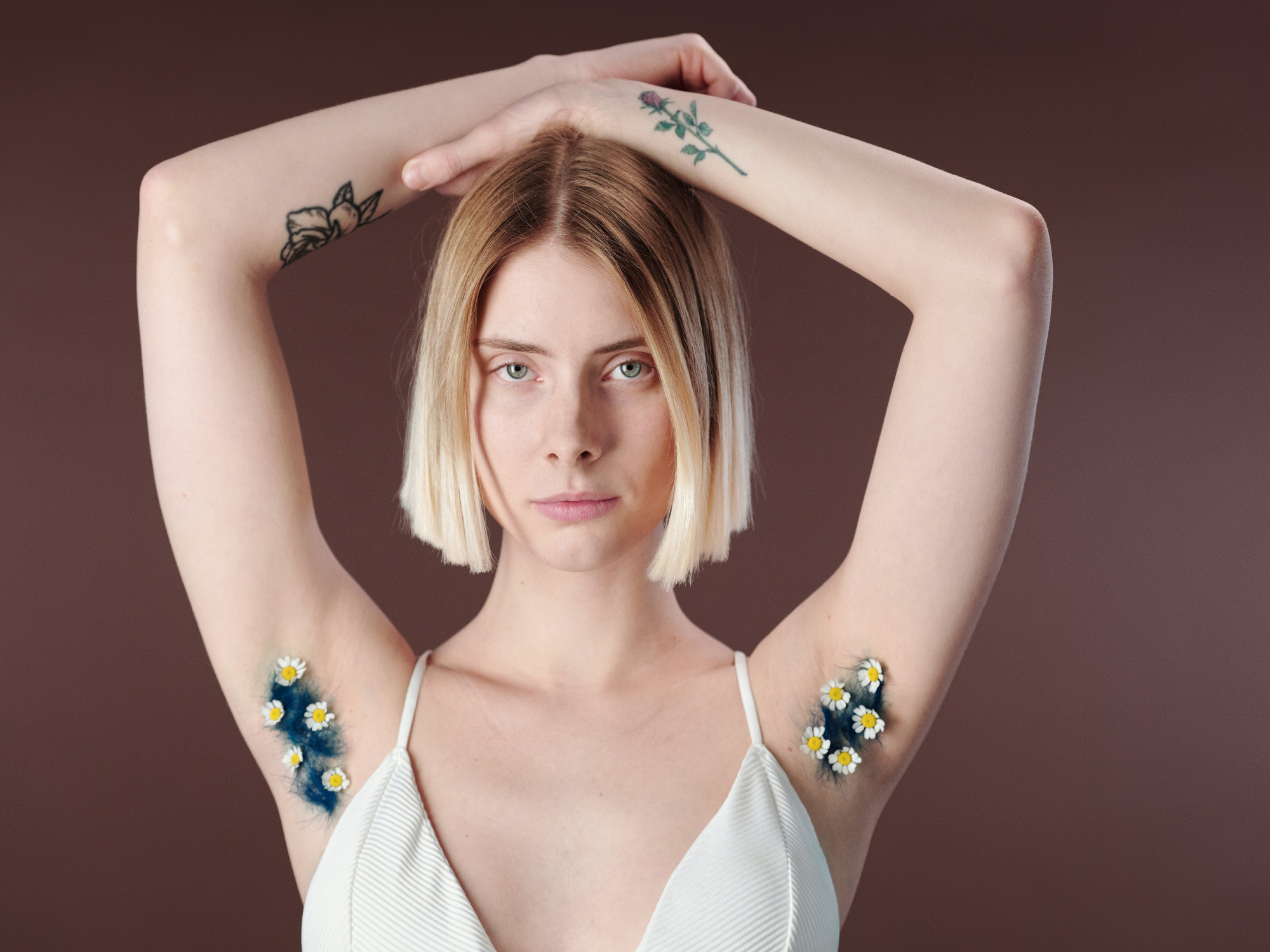 A blonde woman in a white top with her arms above her head and flowers in her armpits.