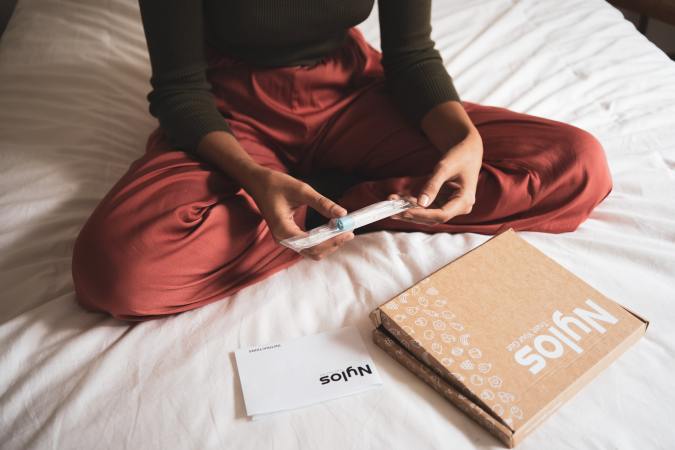 Person in red pajamas holding a pregnancy test on a bed