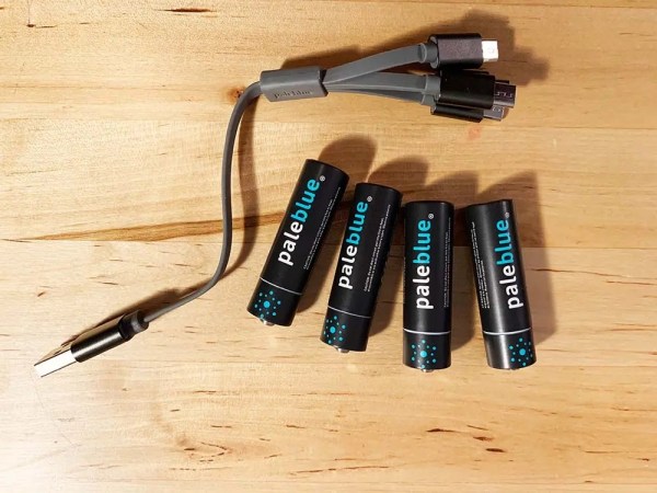  Four Pale Blue AA batteries on a table next to a four-pronged charger.