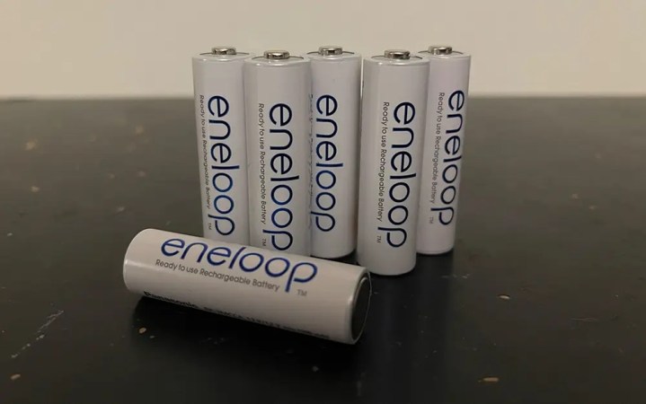  Five AA Panasonic Eneloop batteries standing on a table with a sixth lying down in the foreground in front of them.