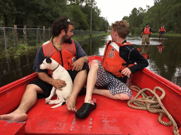 Natural disaster evacuation with two people in life vests on a red boat with a dog